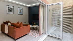Una sala moderna con un sofá, una mesita y un televisor. Hay un ventanal corredero que da a un espacio al aire libre.