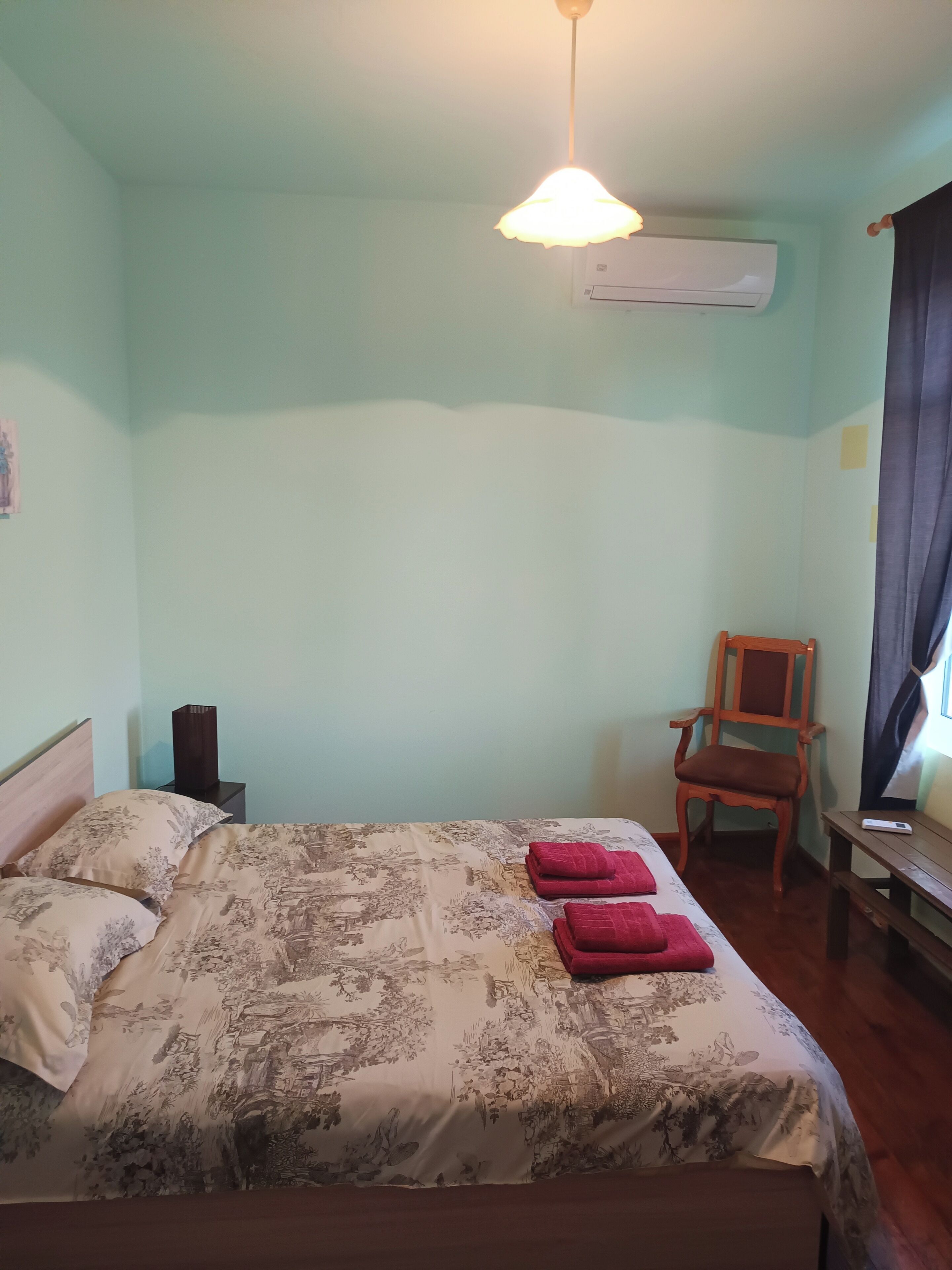 Un dormitorio con una cama, una silla, una mesita de noche y un equipo de aire acondicionado.