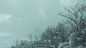Et skilt, der viser 'Kramolin', i et sneklædt landskab med nøgne træer og en overskyet himmel.