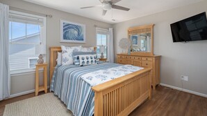 Un dormitorio con una cama de madera, un ventilador de techo, un ventanal con persianas, un televisor de pared y un cuadro sobre la cama.