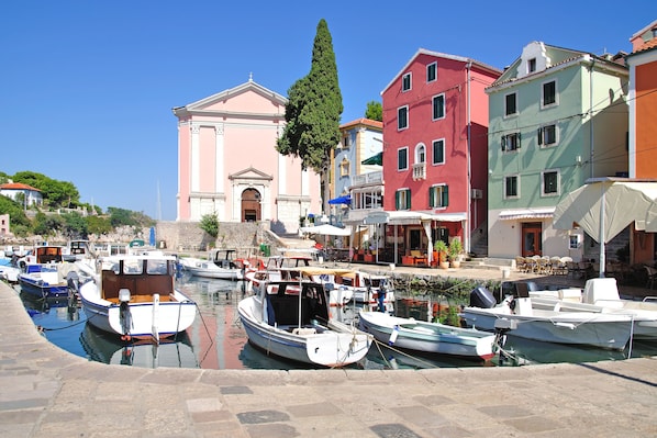 A marina with several boats docked, a pink building with classical architecture, and colorful buildings in the background.