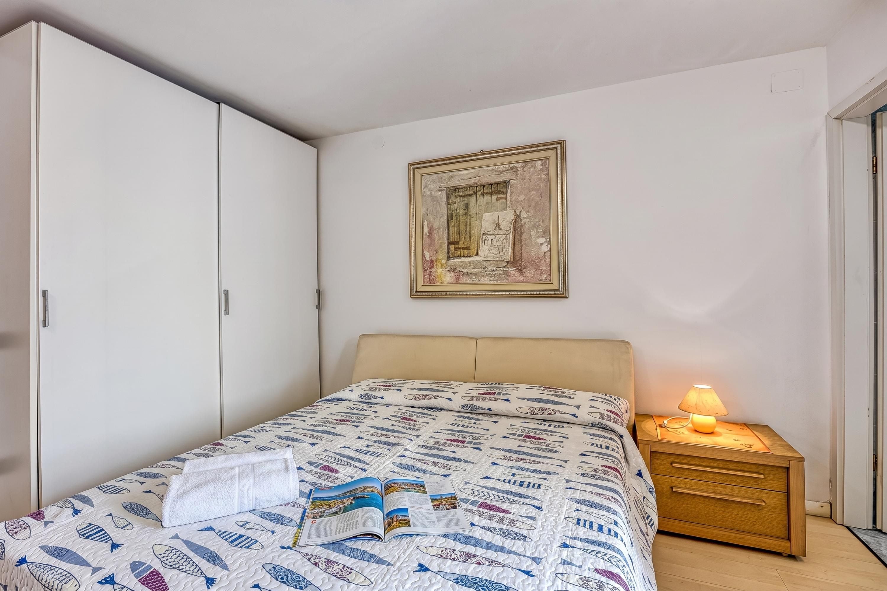 Une chambre à coucher avec un lit, une table de chevet, une armoire et un tableau encadré au mur.