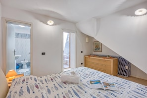 Een slaapkamer met een bed, een kast, een raam en een deur naar een badkamer.