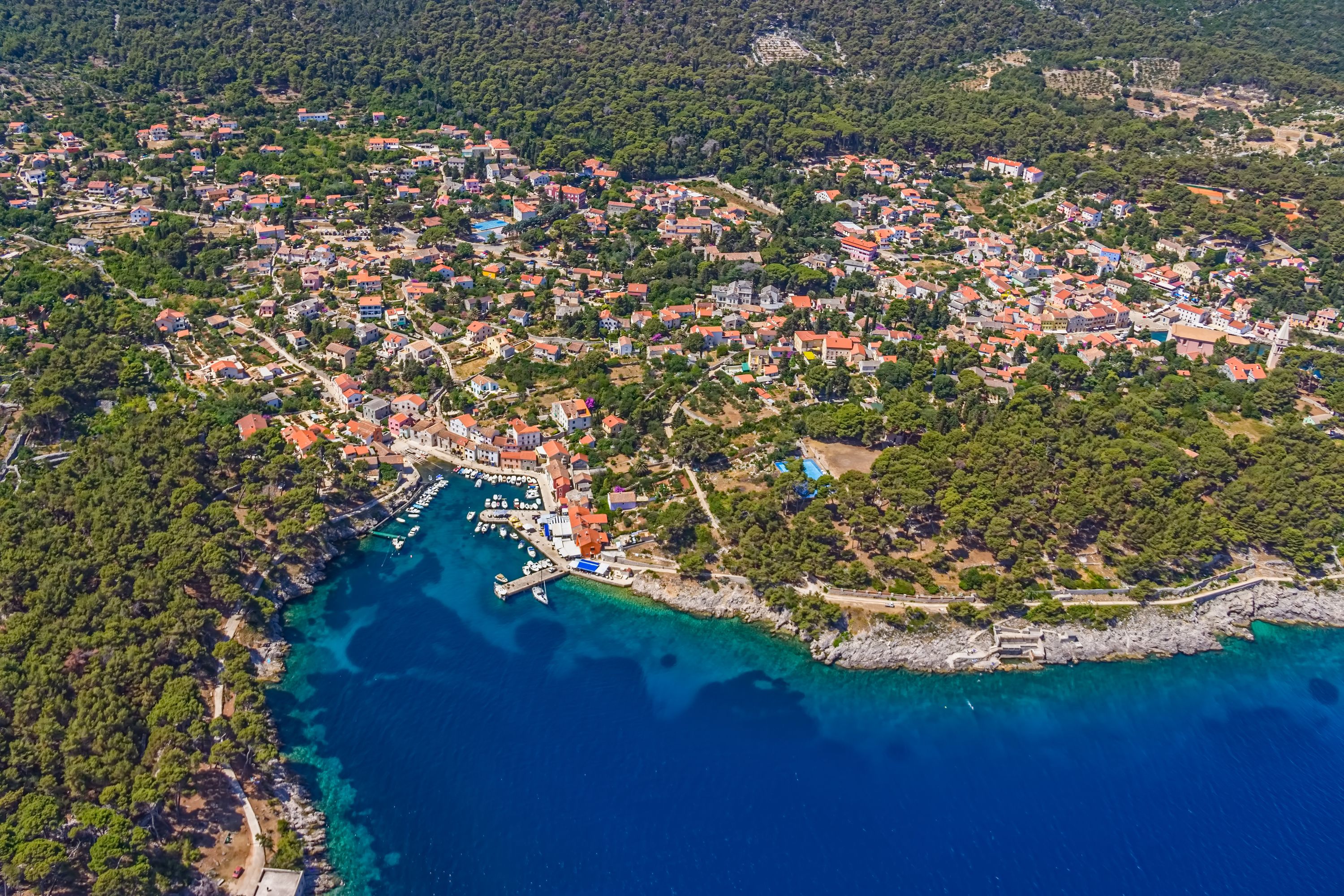 Vue aérienne d’une ville côtière avec des habitations densément regroupées, une marina et des eaux d’un bleu limpide.