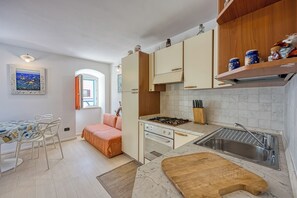 Et kompakt køkken med gasblus, vask og træbordplade. Der er et spiseområde med et bord og stole, samt en sofa.