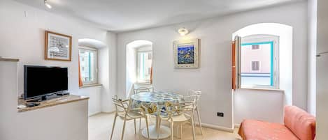 Una sala de estar con televisor, una mesa de comedor con sillas, un sofá y un cuadro en la pared.