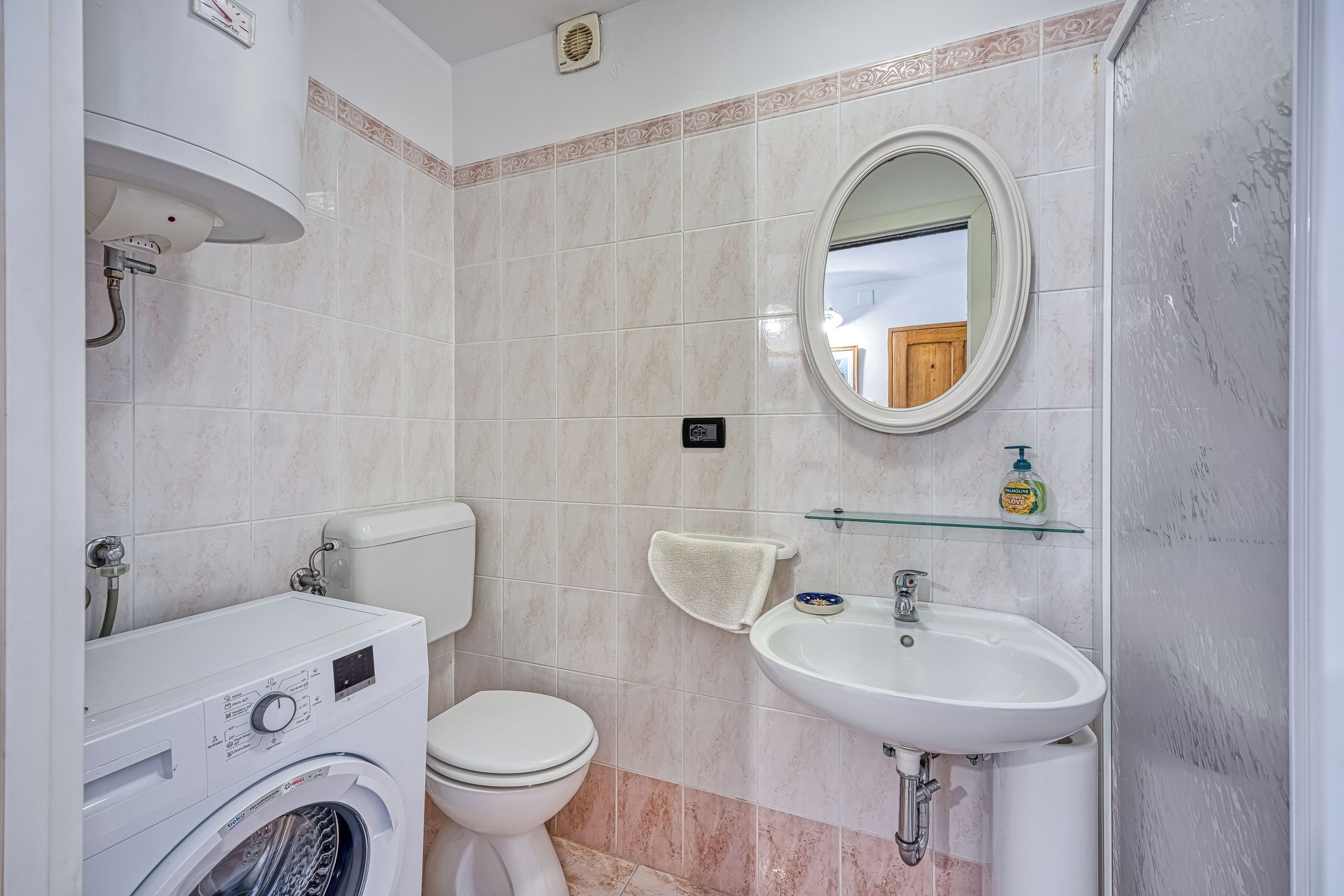 A bathroom with a washing machine, toilet, sink, and a mirror.