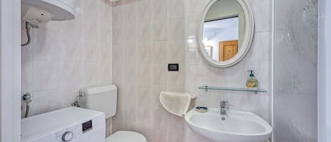 A bathroom with a washing machine, toilet, sink, and a mirror.