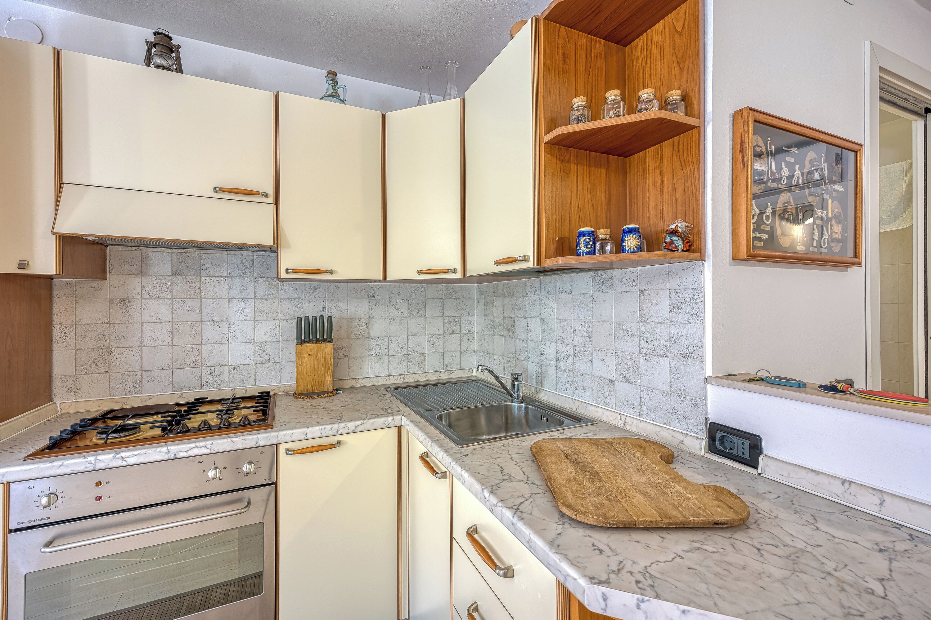 A kitchen with a gas stove, oven, sink, and marble countertop.