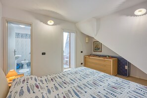 Et soveværelse med seng, kommode, spejl og dør til et badeværelse.