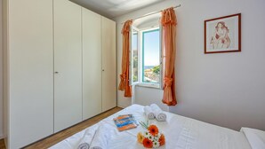 Une chambre à coucher avec un lit, une fenêtre avec des rideaux, une armoire et un tableau encadré au mur.