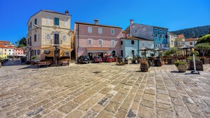 Une place pavée, bordée de bâtiments historiques, avec des terrasses et des voitures garées.