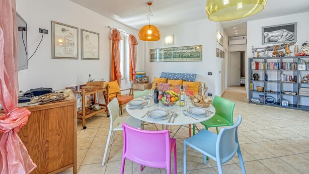 Un coin repas avec une table ronde, des chaises colorées, un buffet en bois et une bibliothèque remplie de livres.