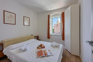 Quarto de hotel com cama, janela com cortinas, um quadro na parede e um livro sobre a cama.