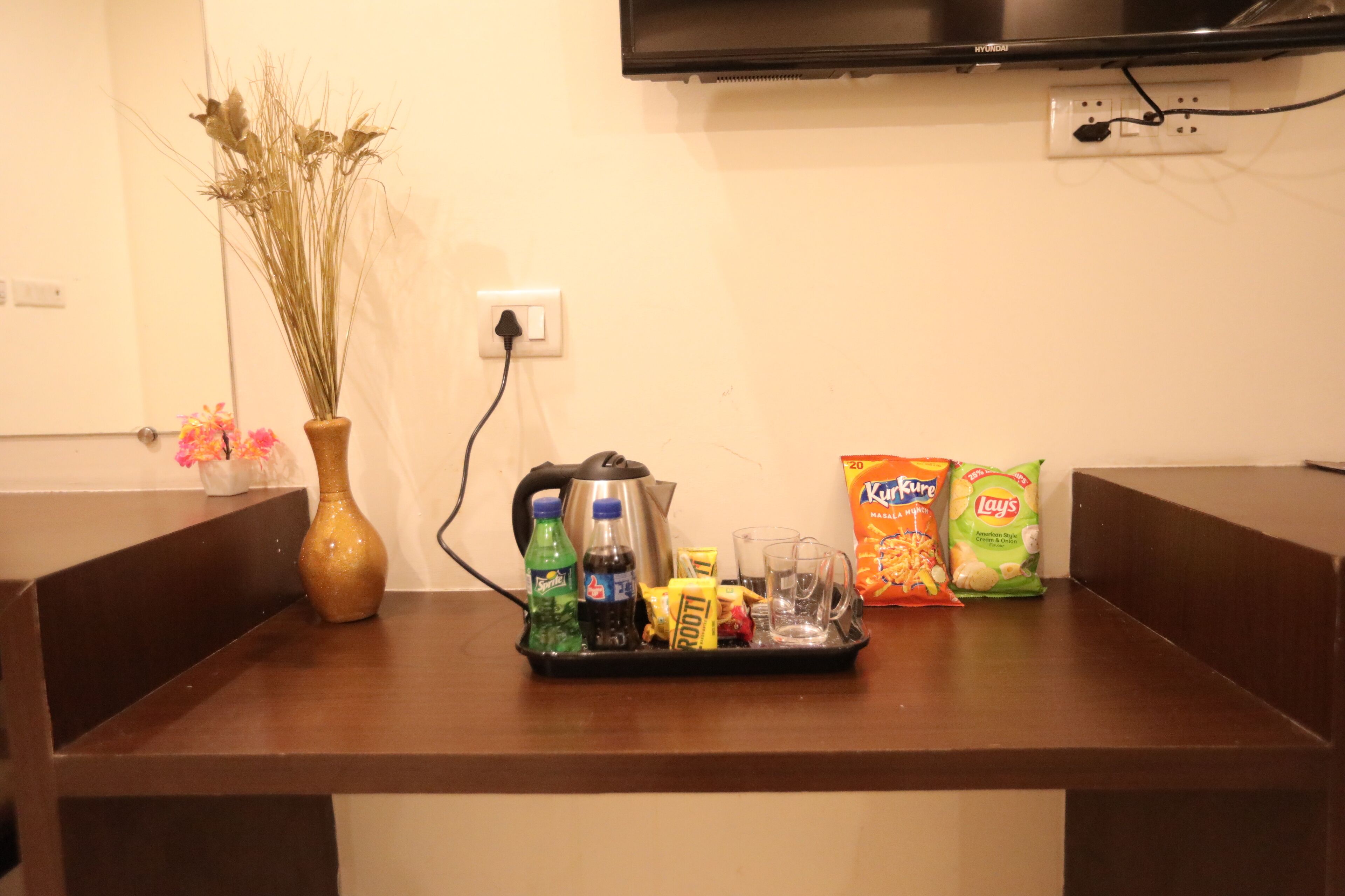 Una encimera de cocina con una cafetera, un jarrón con plantas secas y paquetes de aperitivos.