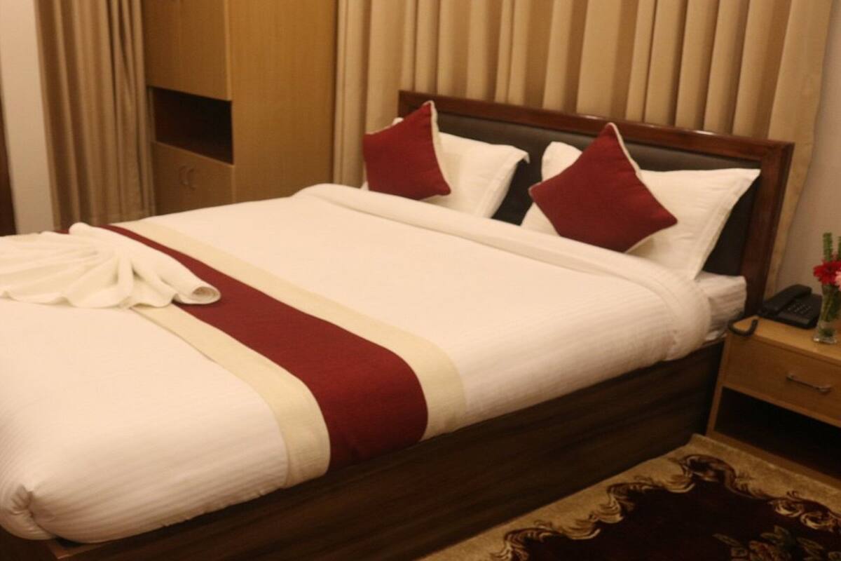 Una cama bien hecha con una colcha blanca y roja, un cabecero de madera y una mesita de noche de madera con un teléfono y una botella.