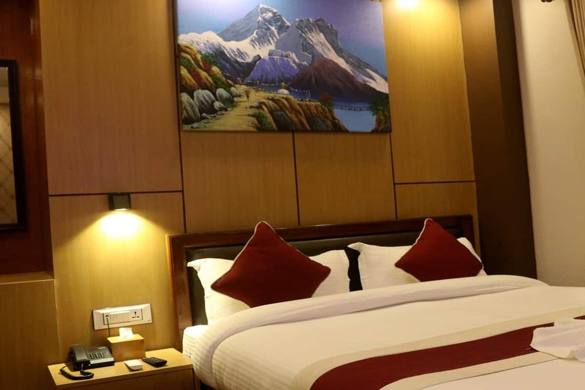 Una habitación de hotel con una cama, un cuadro de un paisaje montañoso, una mesita de noche con un teléfono y una ventana con cortinas.