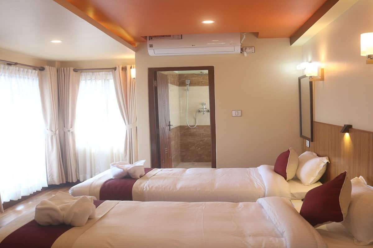 Habitación de hotel con dos camas, televisión, aire acondicionado y zona de ducha.