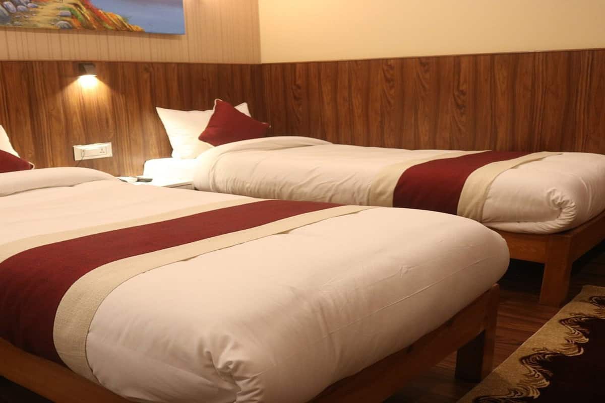 Habitación de hotel con dos camas, cada una con ropa de cama blanca y detalles en rojo, cabeceros de madera y un cuadro en la pared.