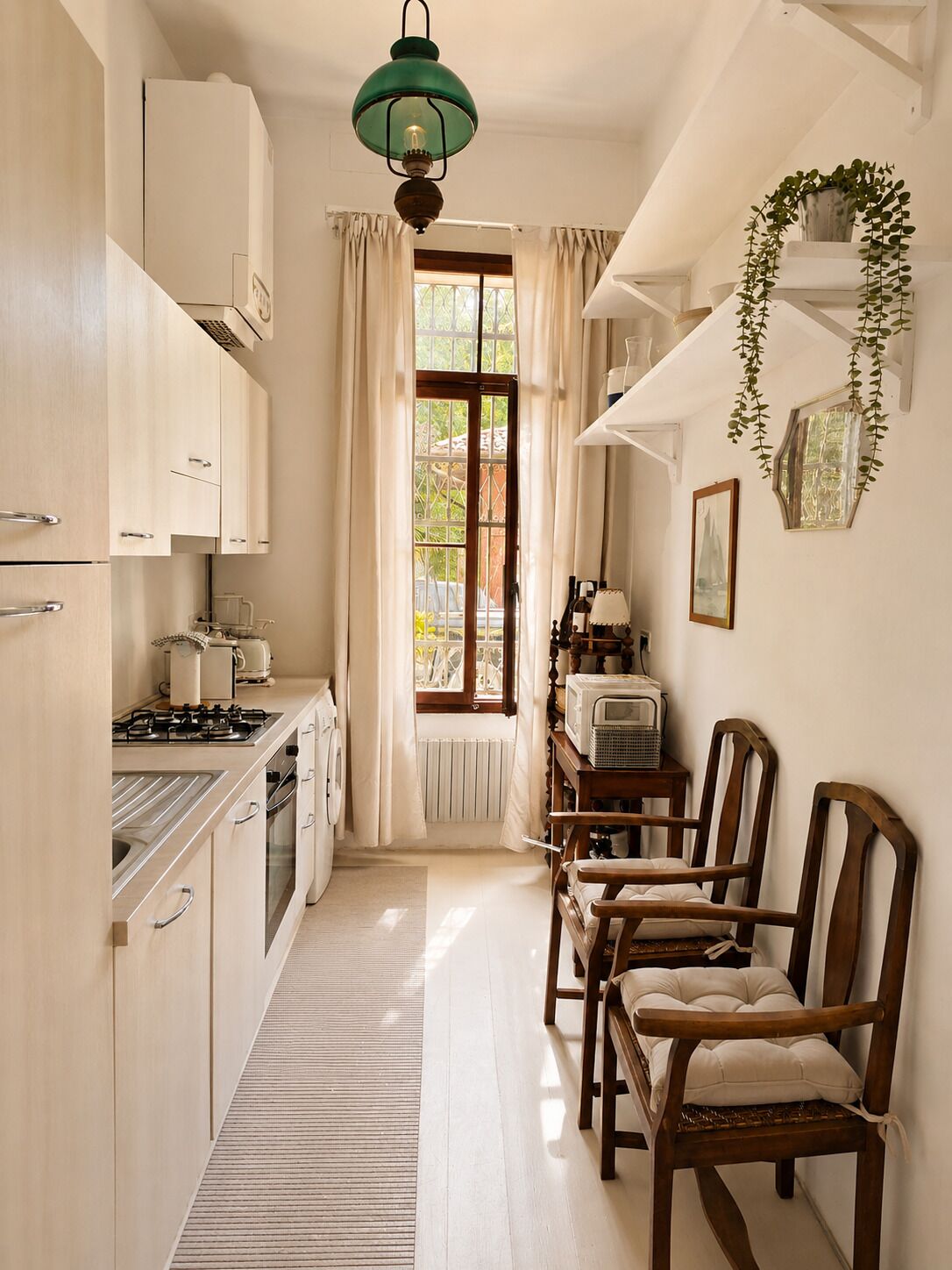 Een smalle keuken met een eetgedeelte, houten kastjes, een fornuis en een hangende lamp.