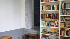 Ein Zimmer mit einem Holzbett, einem kleinen Holztisch und einem weißen Bücherregal voller Bücher.