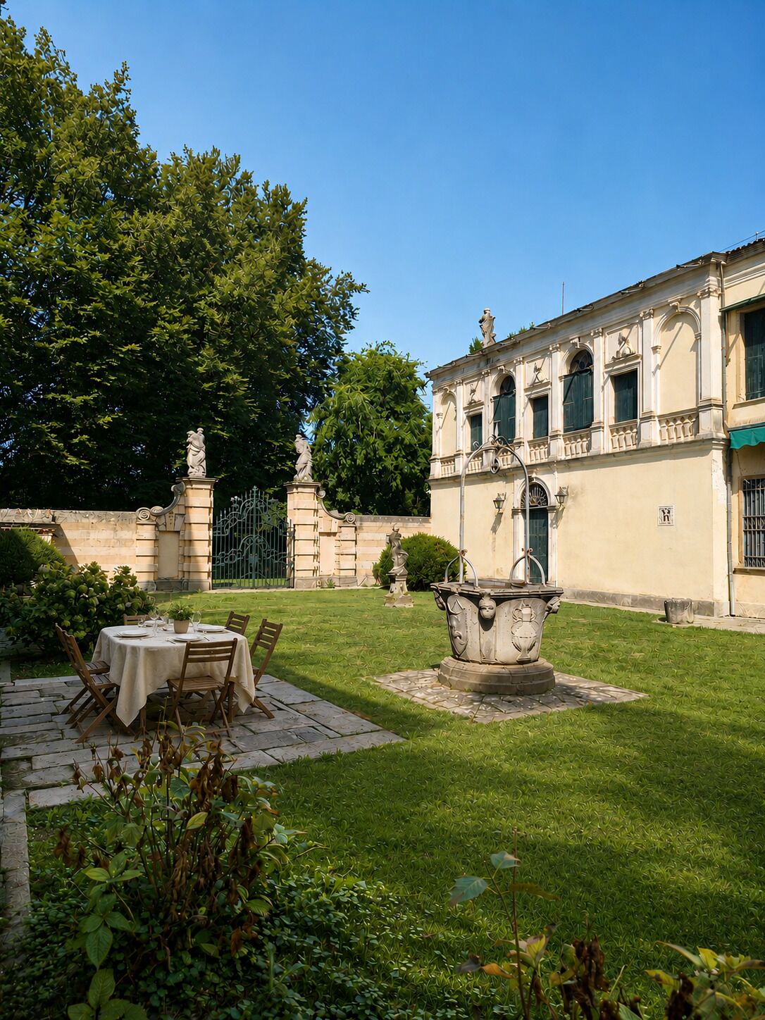 A courtyard with a dining table set for two, surrounded by greenery and a fountain.