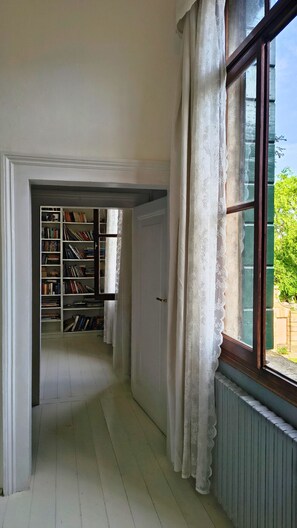 A hallway with a bookshelf, a radiator, and a window with curtains. - Veneto Villa in a vast Park. A Hidden Gem near Padova and Venice.   (Sant'Agostino)