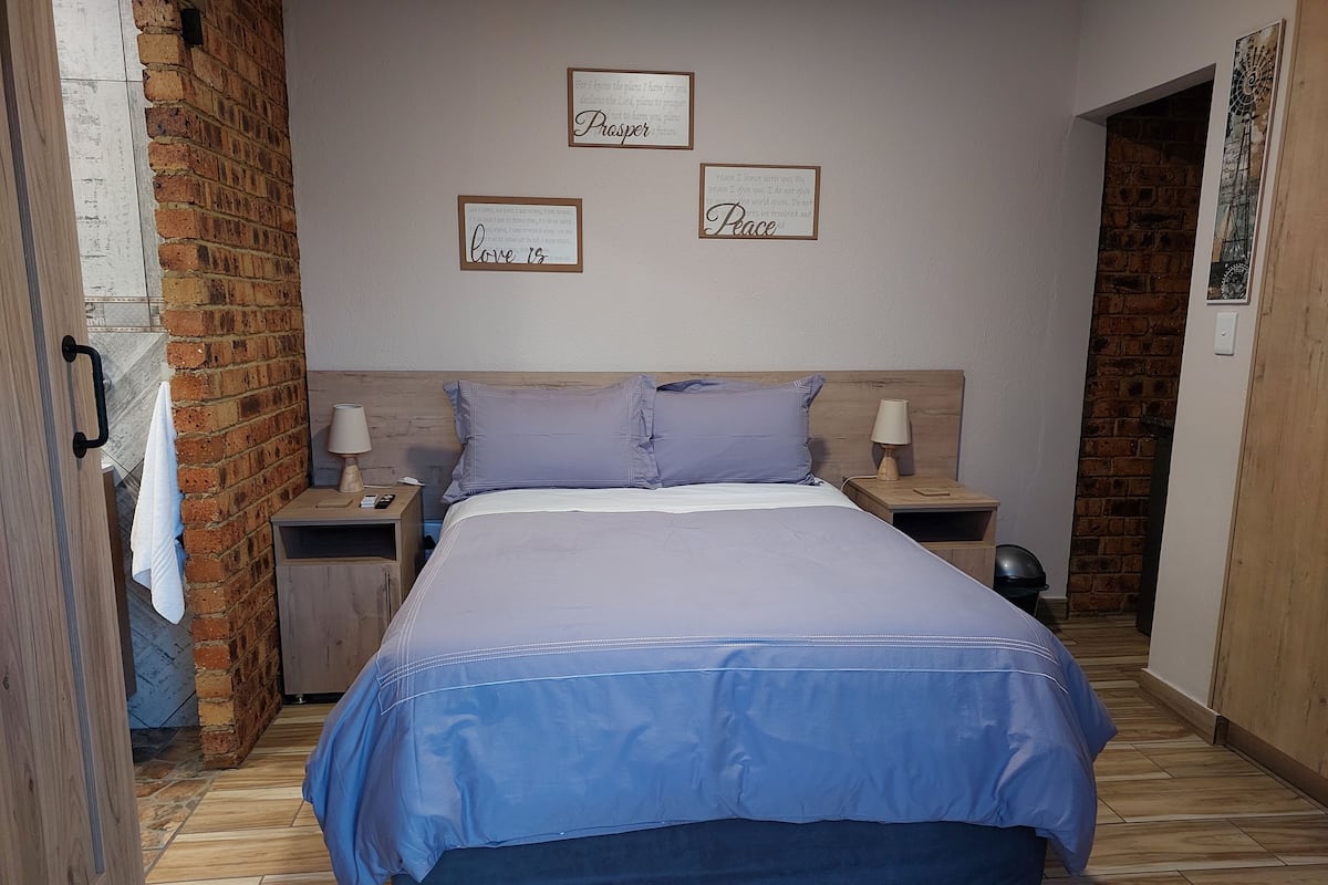 A bedroom with a large bed, two bedside tables, a brick wall, and three framed inspirational quotes on the wall.