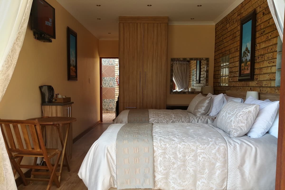 A bedroom with two beds, a wooden chair, a coffee table, and a TV mounted on the wall.