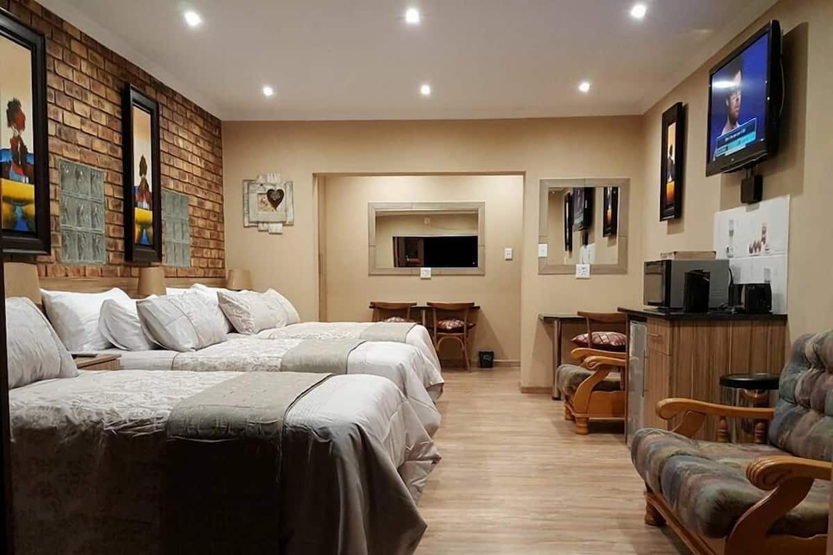 A hotel room with a large bed, a sofa, a TV, and a small kitchen area.