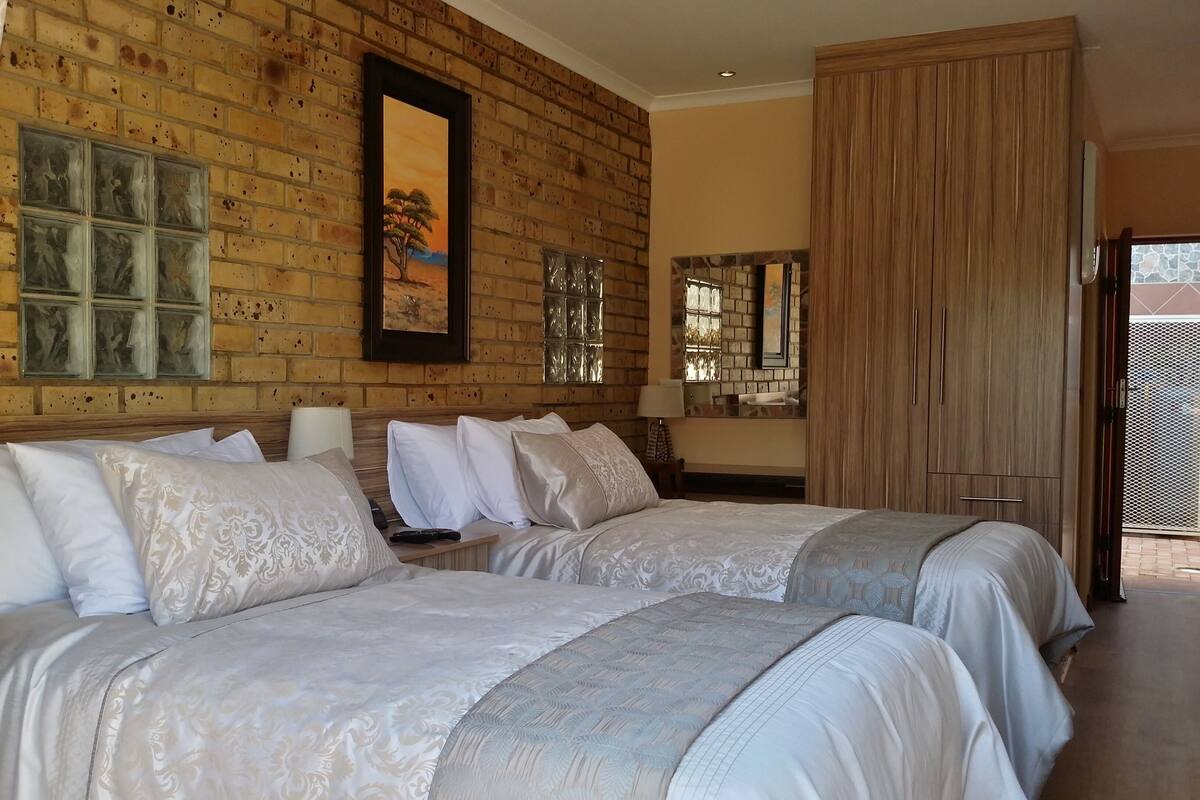 A hotel room with two beds, a brick wall, a painting, and a large window.