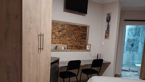 Ett sovrum med en säng, ett skrivbord med två stolar, en tv som är monterad på väggen och ett fönster med en vägg som är dekorerad med tegelstenar.
