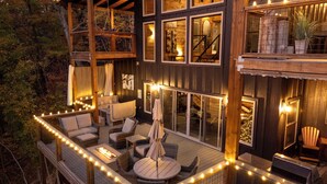 A multi-level outdoor deck with wicker furniture, string lights, and a fire feature.