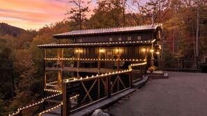 A wooden cabin with multiple levels, string lights, and a stone staircase leading up to the entrance.