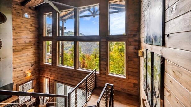 A wooden cabin interior with large windows, a staircase, and a ceiling fan.