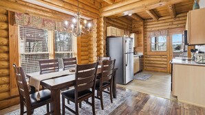 A log cabin interior with a dining area, kitchen, and a chandelier.