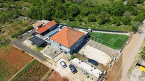 An aerial view of a property with a large building, a fenced sports field, and a parking area.