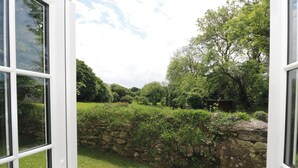 Une porte ouverte donnant sur un jardin avec un mur de pierre, une végétation luxuriante et un ciel dégagé.