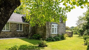 Une maison en pierre avec une pelouse bien entretenue et un chemin de pierre menant à l’entrée.