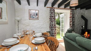 Un coin repas avec une table en bois dressée pour quatre personnes, un canapé vert, une cheminée et un mur en pierre.
