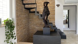Un intérieur moderne avec un escalier adossé à un mur texturé, une statue et une plante en pot.