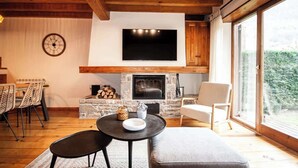 Una sala de estar acogedora con chimenea, un televisor montado arriba y una zona de comedor con sillas y una mesa.