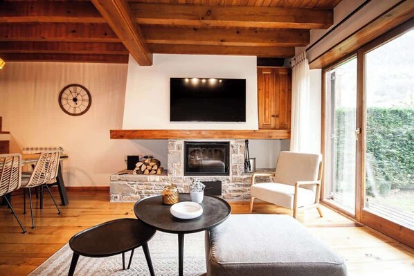 A cozy living room with a fireplace, a television mounted above it, and a dining area with chairs and a table.