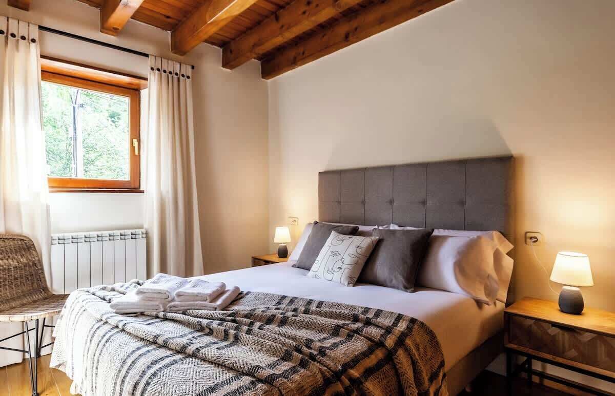 Ein Schlafzimmer mit einem großen Bett, zwei Nachttischen, einem Sessel, einem Fenster mit Vorhängen und einer Heizung.