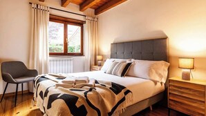 Un dormitorio con cama, una silla, una mesita de noche y un ventanal con cortinas.