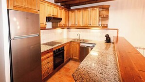Una cocina con armarios de madera, un refrigerador de acero inoxidable, encimera de granito y techo de madera.