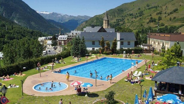 Una piscina rodeada de césped, con un edificio al fondo.