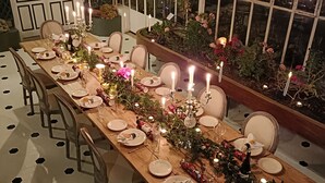 A long wooden dining table set with plates, glasses, and candles, surrounded by chairs.