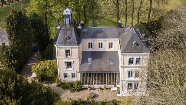 A large, two-story house with a prominent tower, surrounded by a well-maintained garden and trees.