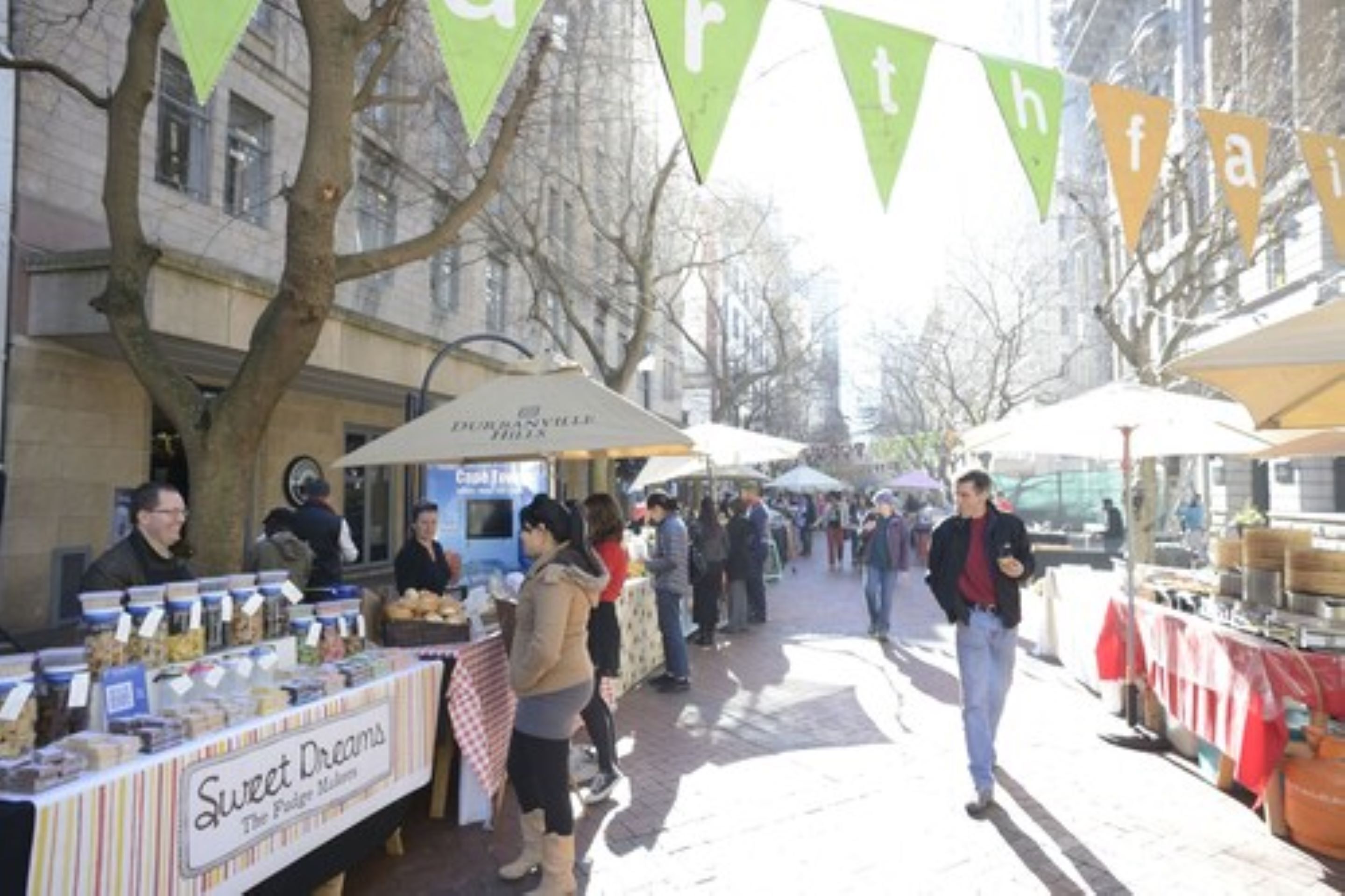 An outdoor market with food stalls and people walking.